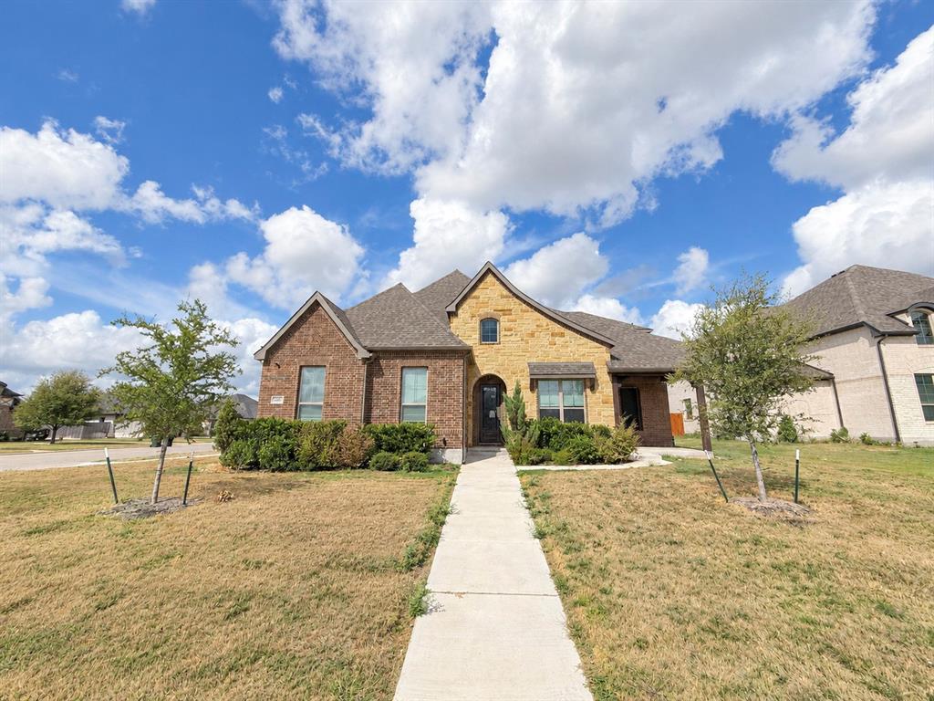 Multi-gable exterior featuring a combination of brick and natural stone masonry, concrete walkway, and shingled roof