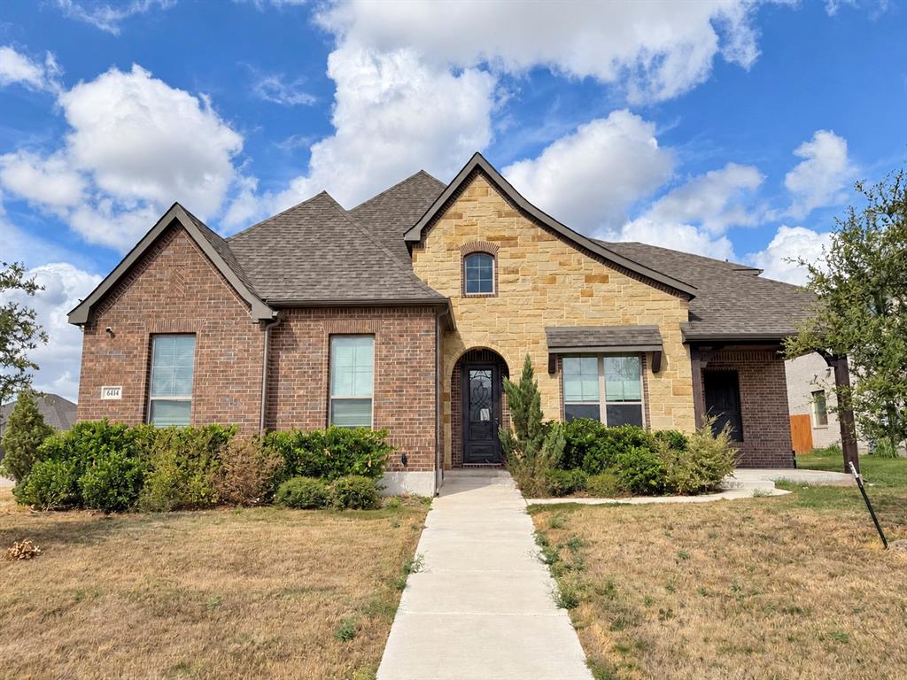 Mixed-masonry exterior featuring brick and natural stone veneer, multi-gabled roofline, and arched entryway with a decorative glass-panel front door