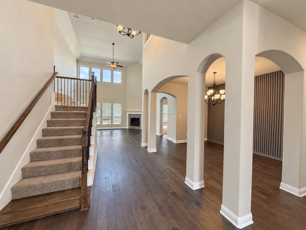 Interior area featuring soaring ceilings, a central staircase with a dark wood-finish railing, dark hardwood flooring, architectural arched openings, and decorative vertical-slat wall paneling