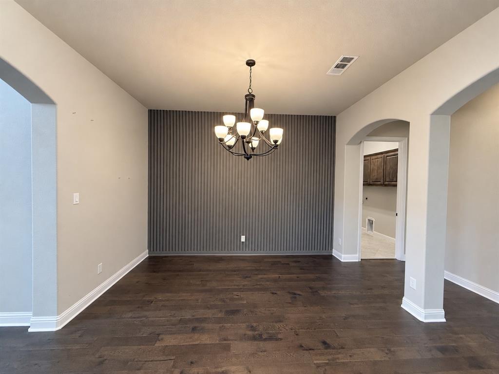 Hardwood flooring, vertical slat accent wall, and multi-arm chandelier featuring frosted glass shades, framed by architectural archways