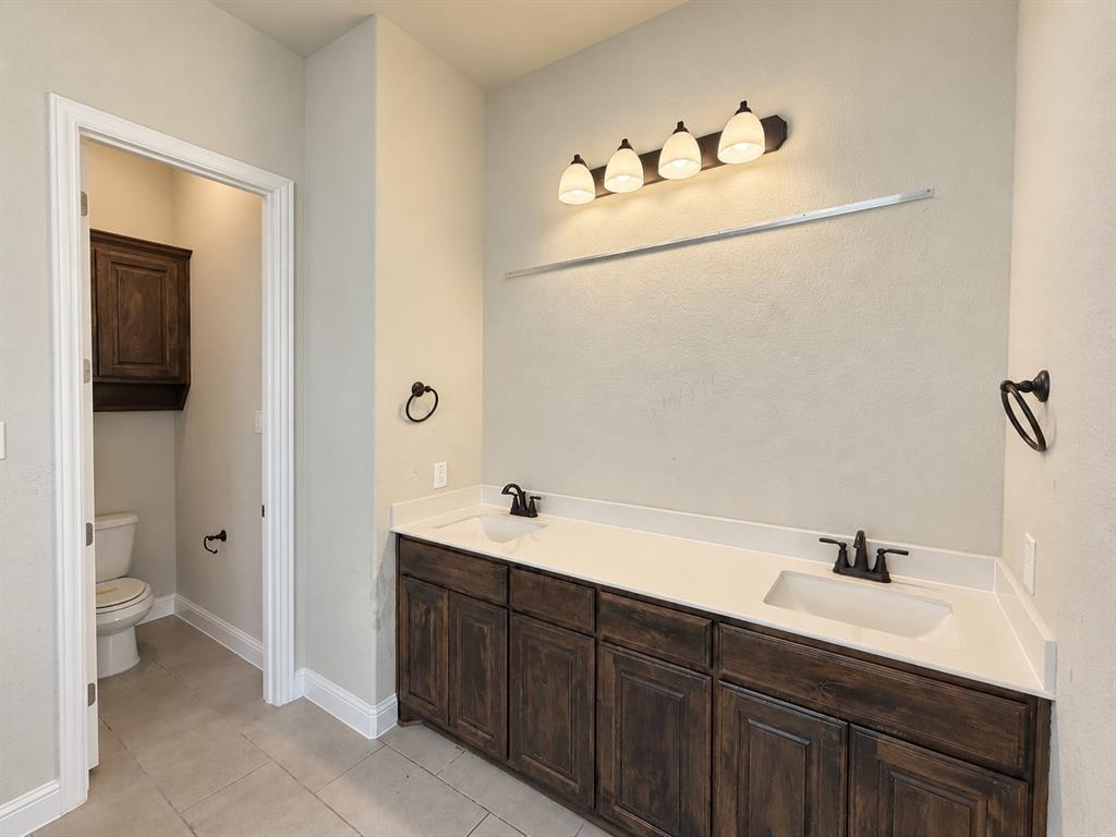 Dual-sink vanity with dark-finish cabinetry, light-toned countertop, oil-rubbed bronze fixtures, and four-light vanity fixture