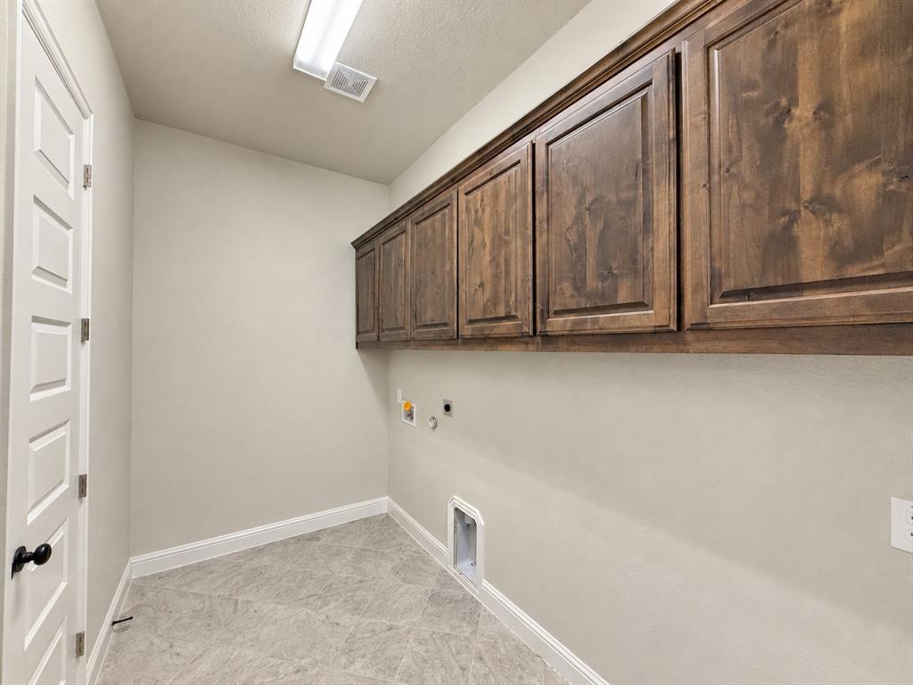 Utility area featuring stained wood cabinetry, grey tile flooring, and a five-panel interior door with matte black hardware