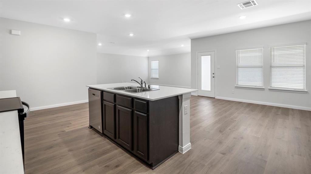Kitchen island featuring a dual basin sink with stainless steel appliances, dark wood cabinetry, and a light-toned countertop