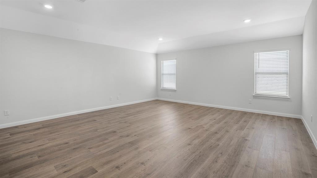 Spacious interior room featuring wood-finish flooring, light gray wall paint, and white baseboards