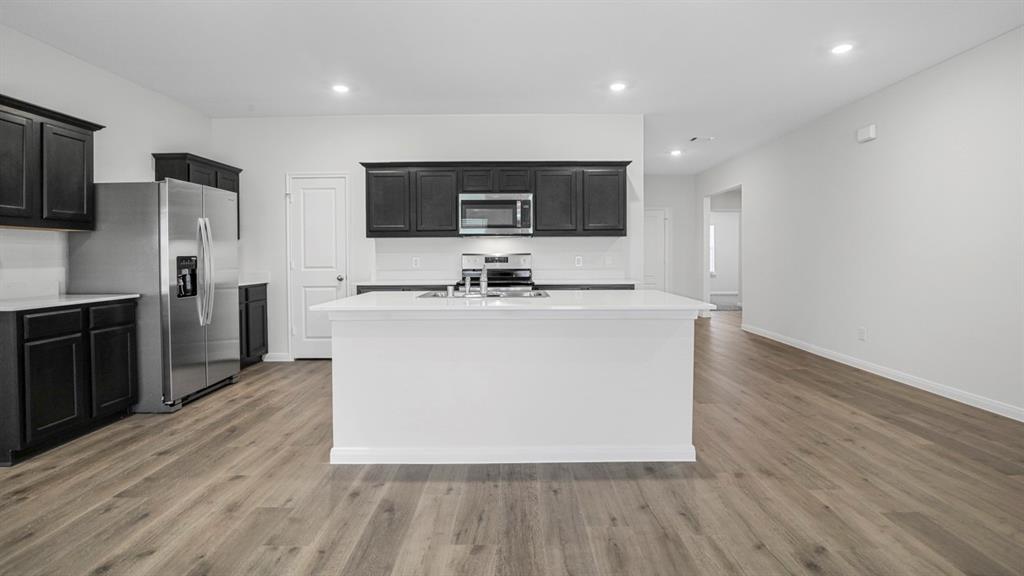 Open-concept kitchen featuring dark wood cabinetry, white countertops, stainless steel appliances, and wood-finish flooring