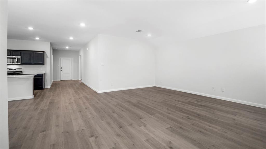 Open-concept living space featuring wood-finish flooring, recessed lighting, and a kitchen with dark cabinetry, light countertops, and stainless steel appliances