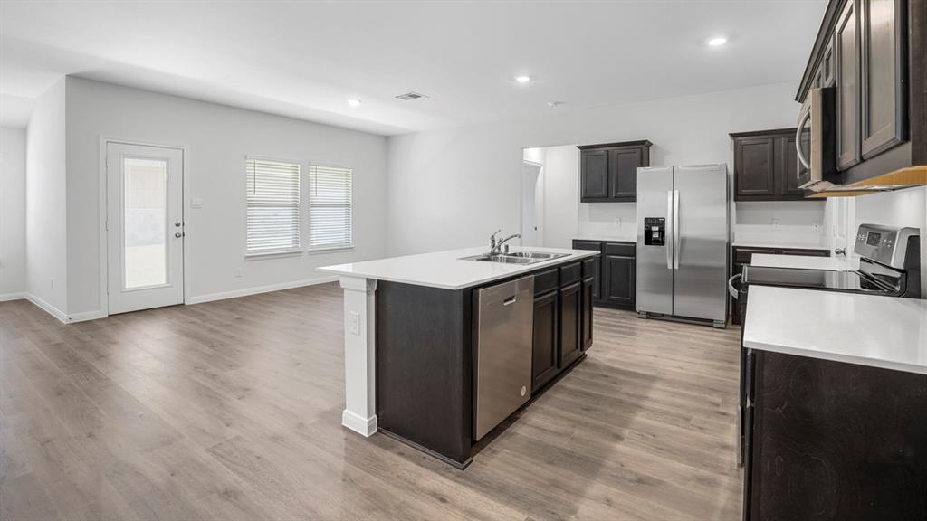 Modern kitchen featuring dark wood cabinetry, white countertops, stainless steel appliances, and wood-finish flooring