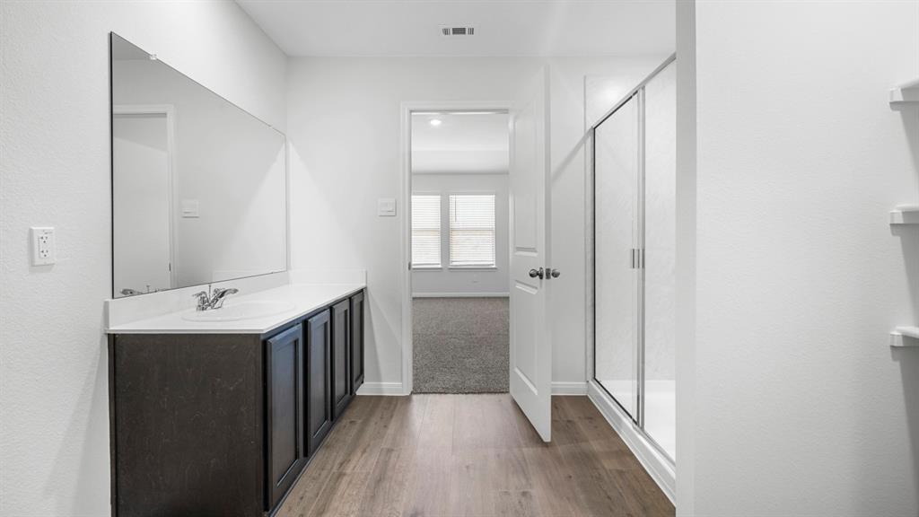 Contemporary bathroom featuring wood-finish flooring and a vanity with a white countertop and dark cabinetry