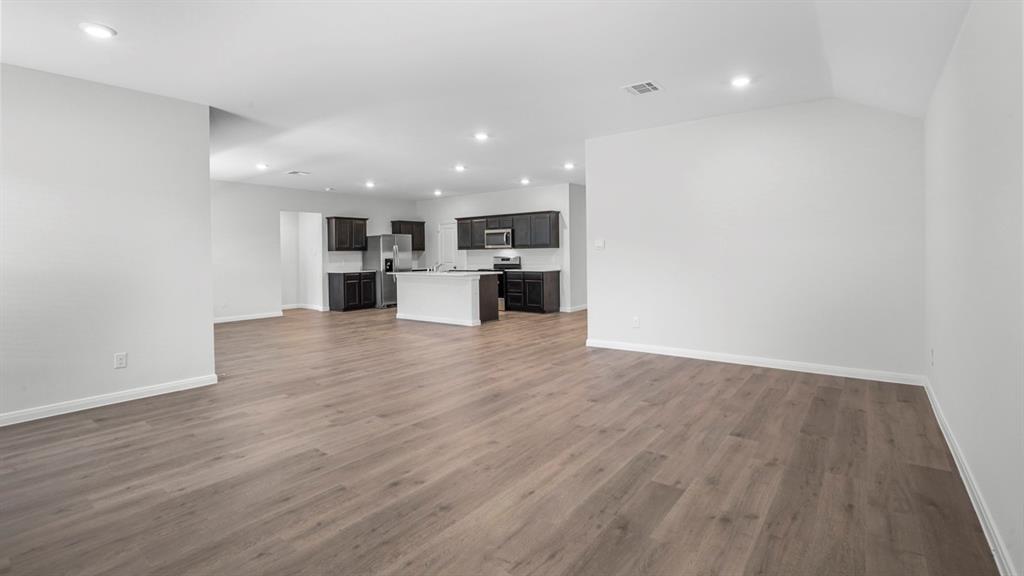 Open-concept living space featuring wood-finish flooring, recessed lighting, and a kitchen with dark cabinetry, light countertops, and a central island