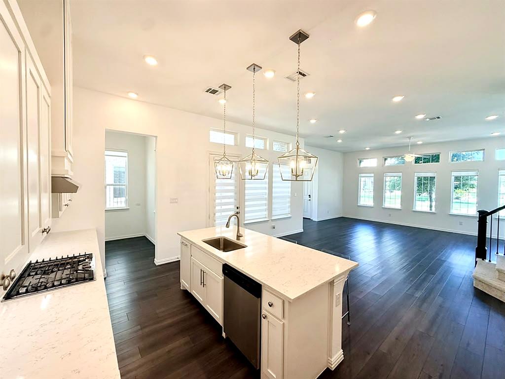 White cabinetry, large center island, quartz-look countertops, gas cooktop, stainless steel appliances, and pendant lighting.