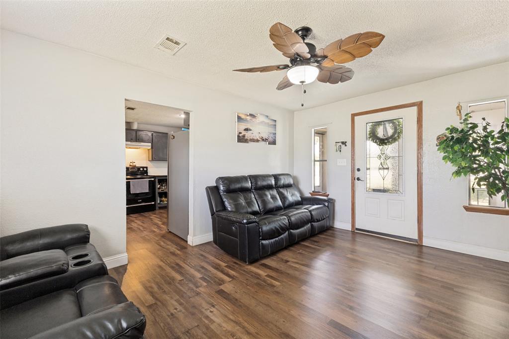 Living area featuring wood-finish flooring, a ceiling fan with leaf-shaped blades, and an exterior door with decorative glass inlay