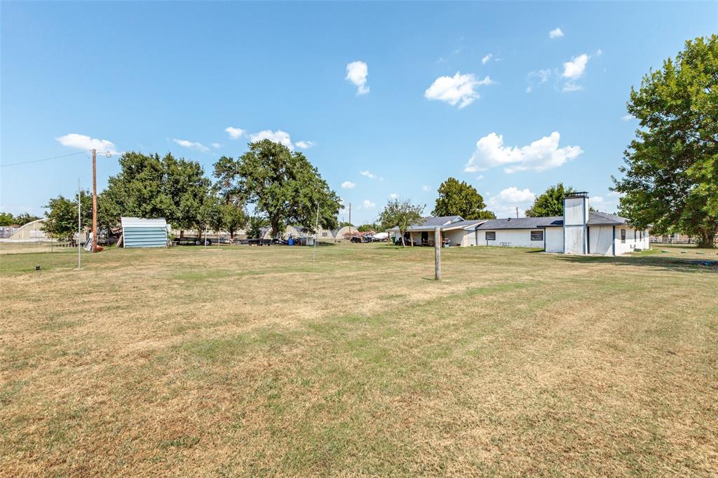 Expansive grass lot featuring mature trees, a detached metal storage structure, and a masonry exterior chimney