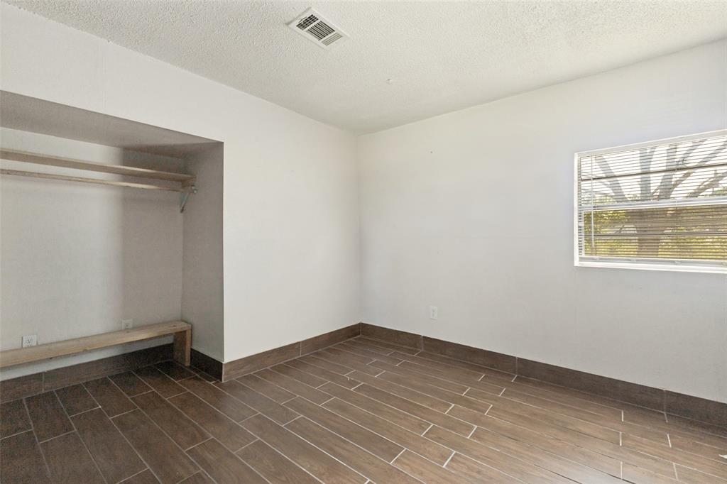 Interior space featuring wood-finish tile flooring, white walls, a built-in recessed closet with shelving, and a horizontal window with installed blinds