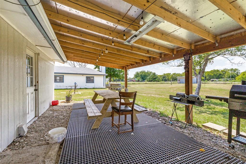 Covered patio featuring an exposed timber-beam ceiling, reflective paneling, and a grid-style metal flooring surface