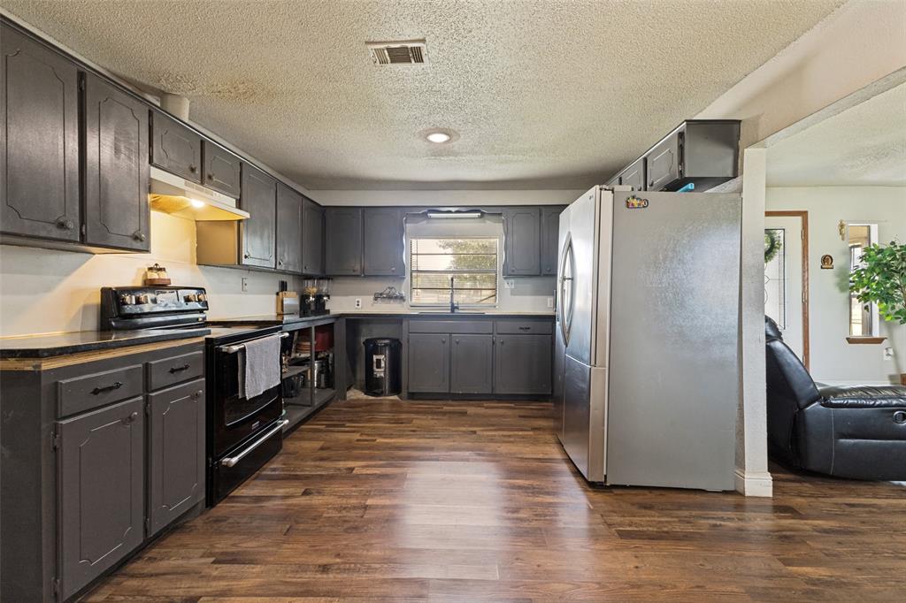 Kitchen featuring dark-finish cabinetry, stainless steel refrigerator, black electric range, wood-finish flooring, and natural light from a window over the sink