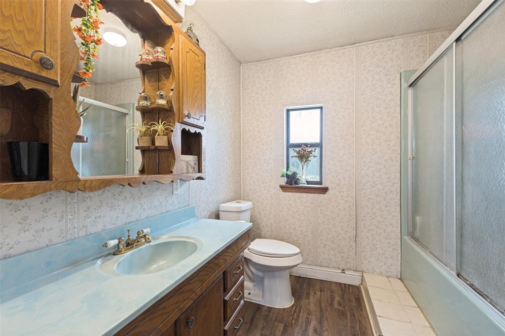 Wood-finish cabinetry featuring built-in shelving, integrated basin with metal hardware, tub and shower combination with sliding glass doors, and wood-finish flooring