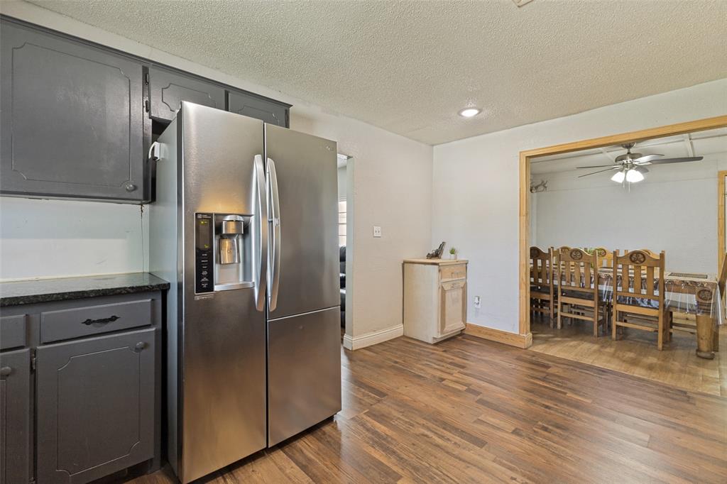 Kitchen featuring charcoal-toned cabinetry, stone-surface countertops, and a stainless-steel refrigerator, with wood-finish flooring extending into the surrounding area