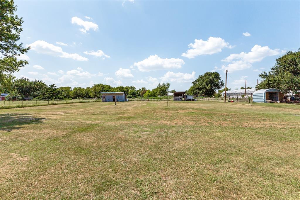 Expansive open lot featuring grass landscape, metal storage outbuildings, and wire perimeter fencing