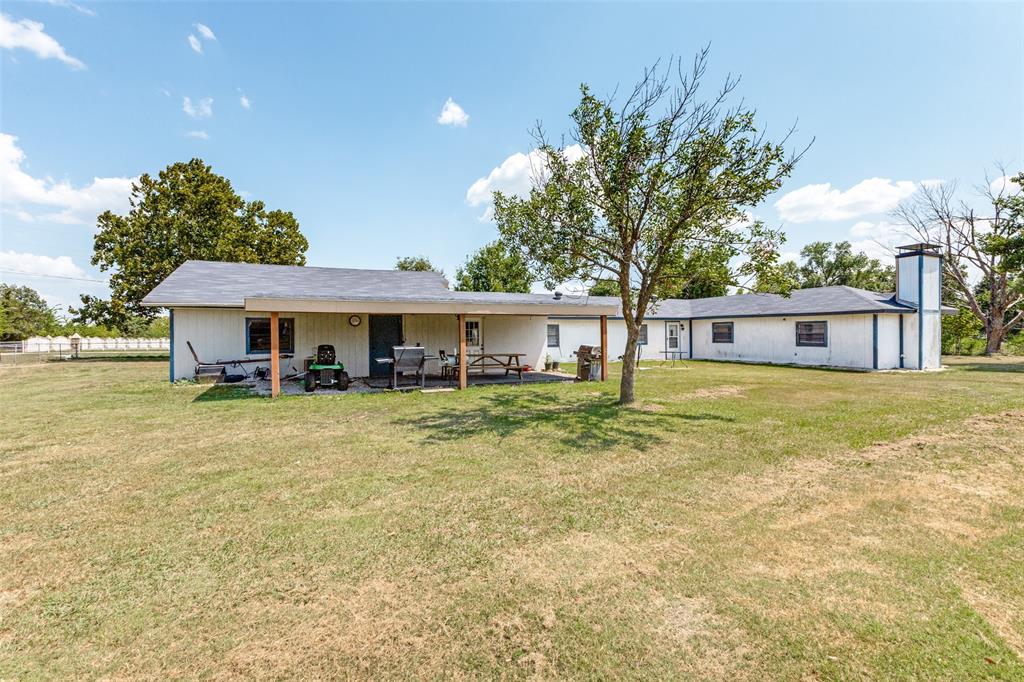 Single-story ranch exterior featuring a covered patio, exterior chimney, vertical siding, and expansive grounds