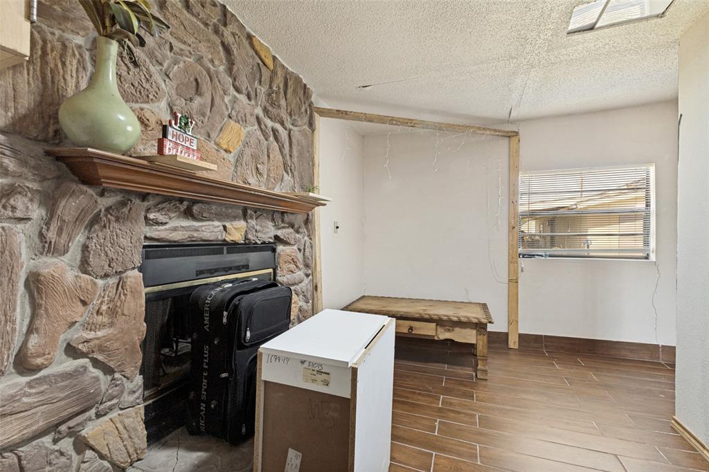 Floor-to-ceiling natural stone fireplace with a wood mantel, wood-finish tile flooring, and window with horizontal blinds