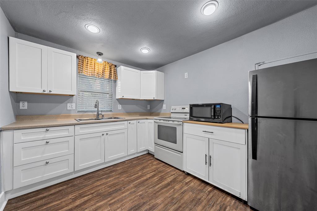 Kitchen featuring white shaker-style cabinetry, wood-finish flooring, recessed lighting, and a stainless steel sink with a high-arch faucet Kitchen featuring white shaker-style cabinetry, wood-finish flooring, recessed lighting, and a stainless steel sink with a high-arch faucet