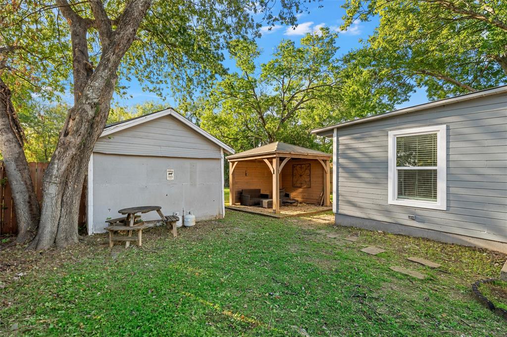 Outdoor space featuring a wooden gazebo, detached storage structure, siding exterior, mature trees, and grass lawn