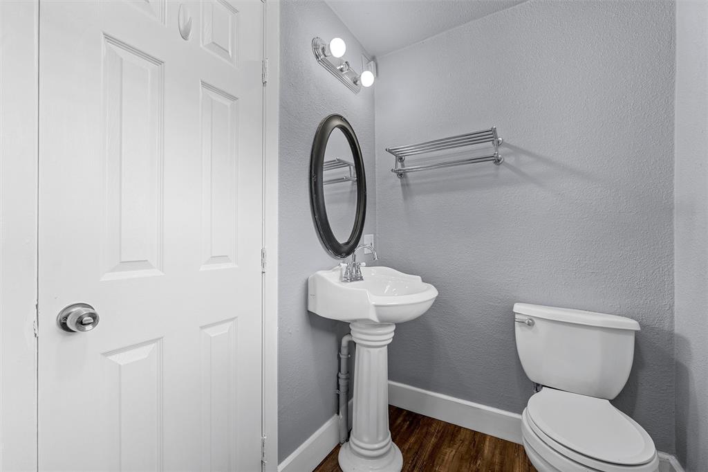 White pedestal sink with chrome faucet, oval wall-mounted mirror, metal wall-mounted towel rack, and wood-finish flooring