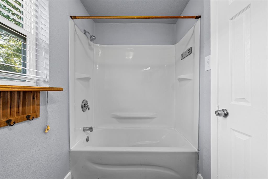 Full-height acrylic tub surround with integrated shelving, chrome shower hardware, window with horizontal blinds, and a built-in wooden wall-mounted organizer Full-height acrylic tub surround with integrated shelving, chrome shower hardware, window with horizontal blinds, and a built-in wooden wall-mounted organizer