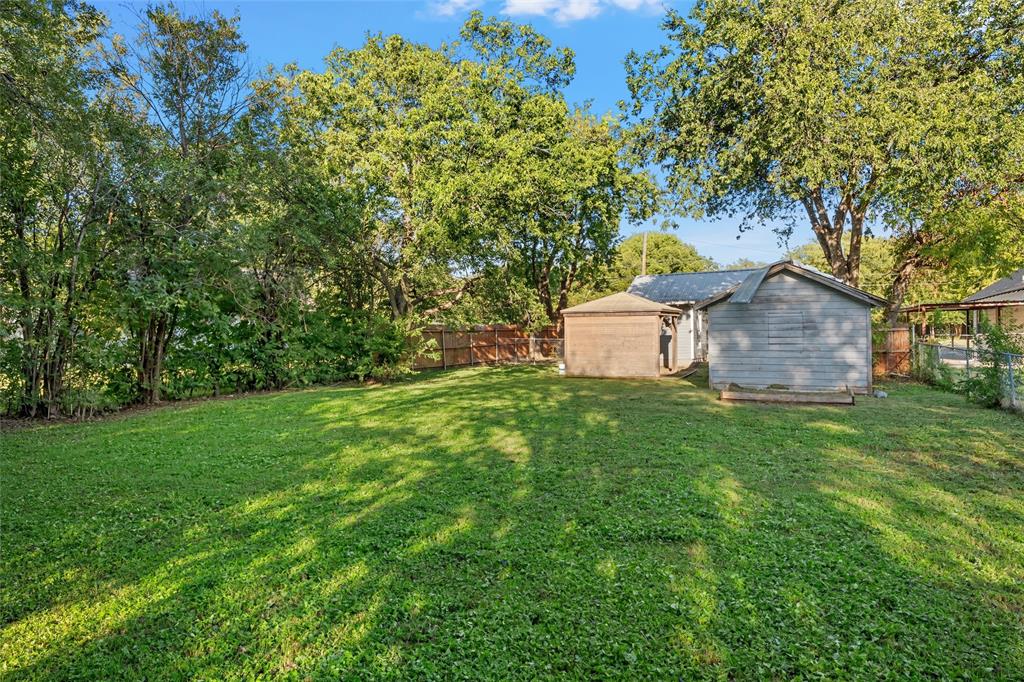 Expansive backyard featuring a large grass lawn, mature trees, and wooden perimeter fencing