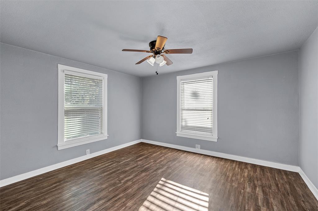 Room featuring wood-finish flooring, two windows with blinds, and a ceiling-mounted light fixture with fan Room featuring wood-finish flooring, two windows with blinds, and a ceiling-mounted light fixture with fan