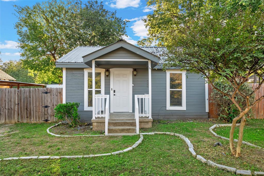 Exterior featuring grey horizontal lap siding, a metal roof, a covered front porch with white railings, and decorative stone garden edging Exterior featuring grey horizontal lap siding, a metal roof, a covered front porch with white railings, and decorative stone garden edging