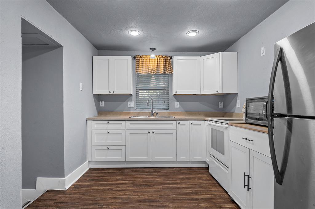 Kitchen featuring white shaker-style cabinetry, solid-surface countertops, recessed lighting, stainless steel refrigerator, and wood-finish flooring Kitchen featuring white shaker-style cabinetry, solid-surface countertops, recessed lighting, stainless steel refrigerator, and wood-finish flooring