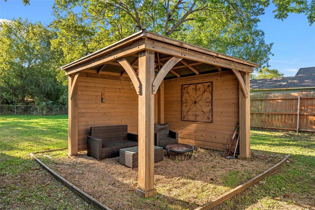 Wood-frame gazebo featuring horizontal plank siding, decorative wood support brackets, and a fenced backyard setting
