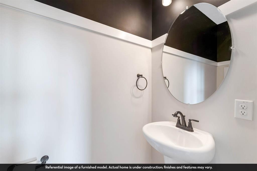 Wall-mounted white pedestal sink with a dark metal two-handle faucet, oval wall mirror, and contrast wall trim with dark upper-wall detailing