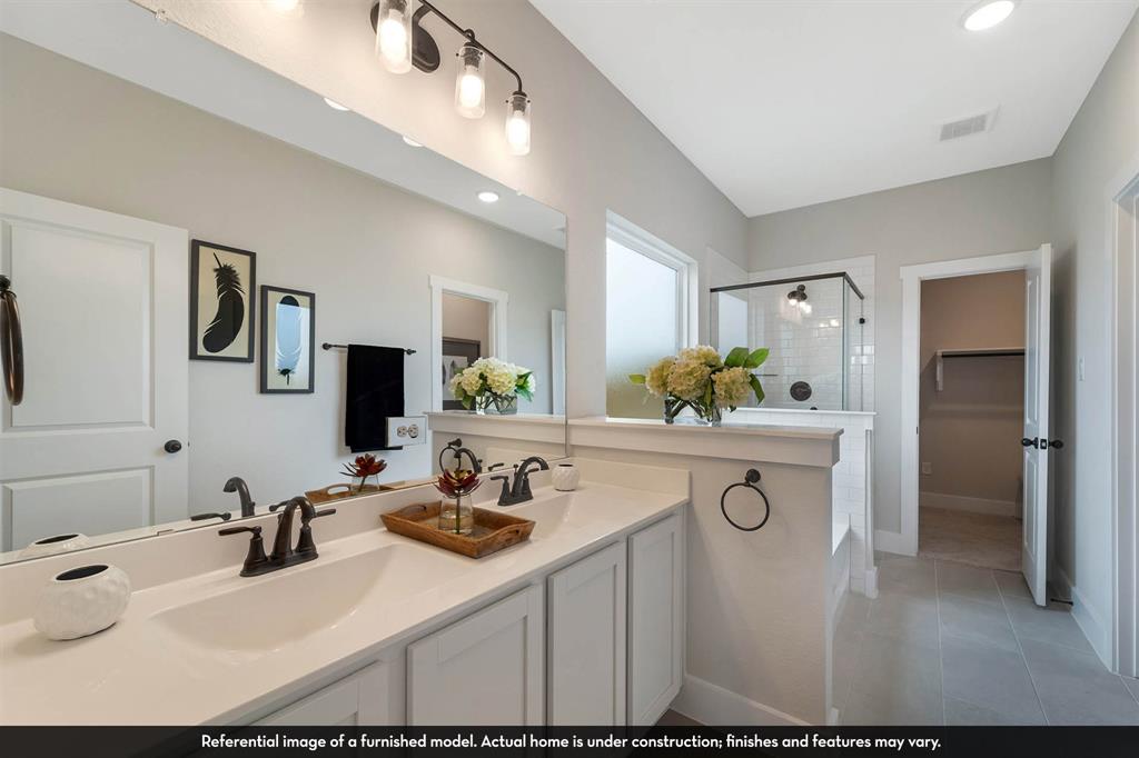 Dual-sink vanity with light-tone cabinetry, stone-surface countertop, and matte black plumbing fixtures, complemented by a large wall-mounted mirror, recessed lighting, and a glass-enclosed shower