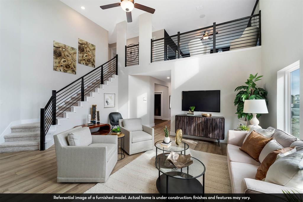 Two-story living area featuring vaulted ceilings, wood-finish flooring, a mezzanine overlook with black horizontal metal railings, and a staircase with matching metal railing