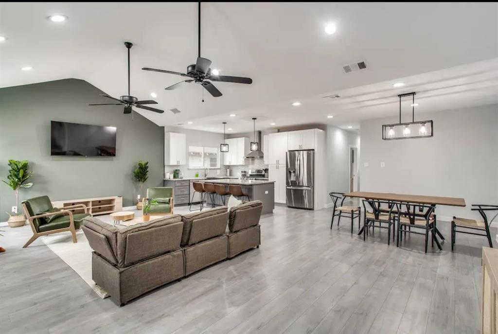 Open-concept interior featuring vaulted ceilings, wood-finish flooring, recessed lighting, and a kitchen equipped with a central island and stainless steel appliances Open-concept interior featuring vaulted ceilings, wood-finish flooring, recessed lighting, and a kitchen equipped with a central island and stainless steel appliances