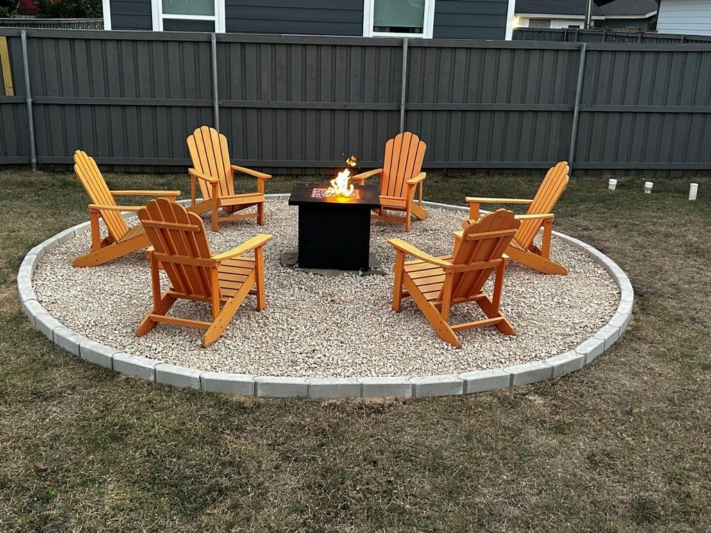 Circular outdoor fire pit area featuring a gravel base, concrete paver edging, and a permanent metal fire pit enclosure