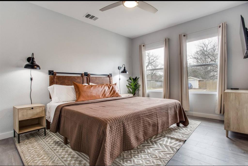 Wood-finish flooring, dual wall-mounted matte black light fixtures, ceiling fan with integrated light, and large windows with natural light Wood-finish flooring, dual wall-mounted matte black light fixtures, ceiling fan with integrated light, and large windows with natural light