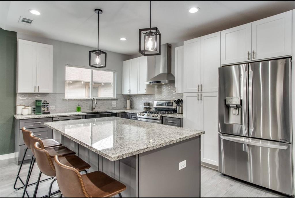 Kitchen featuring a central island with stone-finish countertops, stainless steel appliances, white upper cabinetry, grey lower cabinetry, and glass-paneled pendant lighting Kitchen featuring a central island with stone-finish countertops, stainless steel appliances, white upper cabinetry, grey lower cabinetry, and glass-paneled pendant lighting