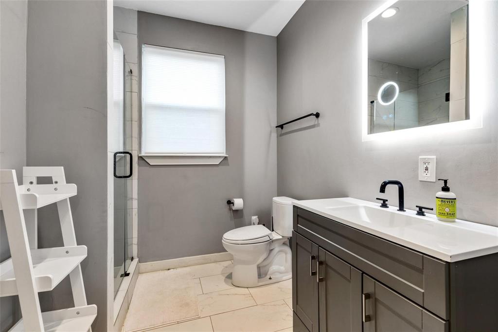 Bathroom featuring a dark gray vanity with a white countertop, matte black fixtures, an integrated LED-backlit mirror, and tile flooring