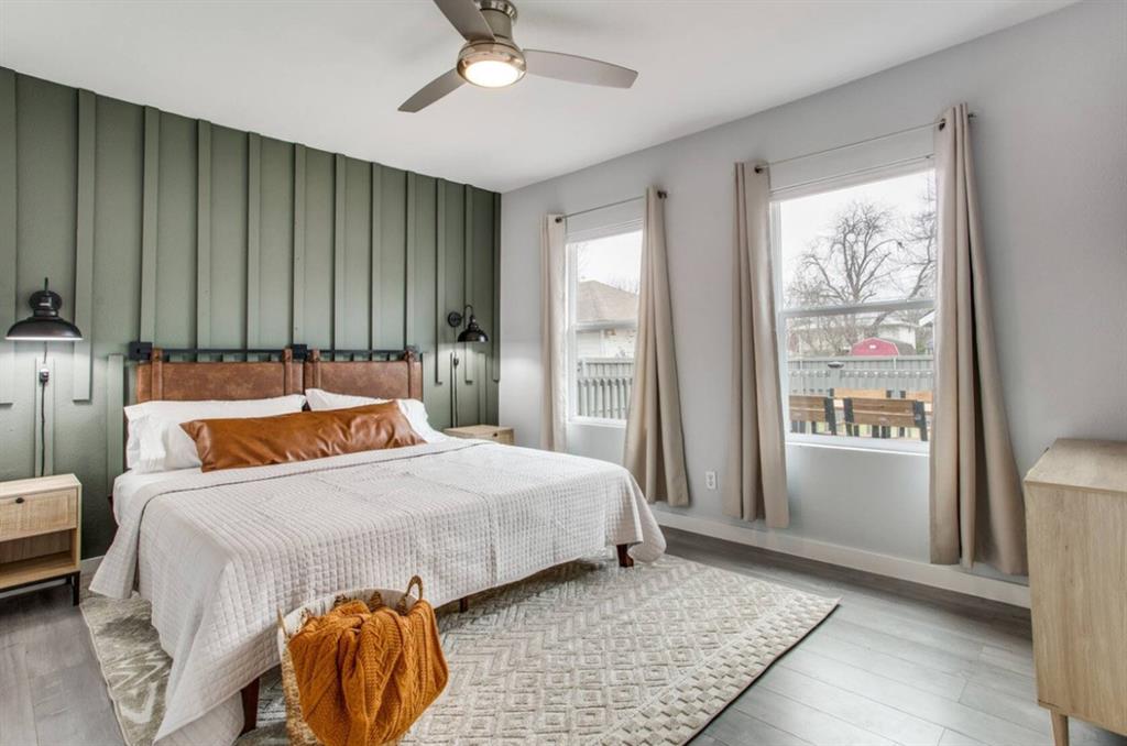 Vertical board-and-batten accent wall, wood-finish flooring, ceiling fan with integrated lighting, and dual wall-mounted sconces Vertical board-and-batten accent wall, wood-finish flooring, ceiling fan with integrated lighting, and dual wall-mounted sconces