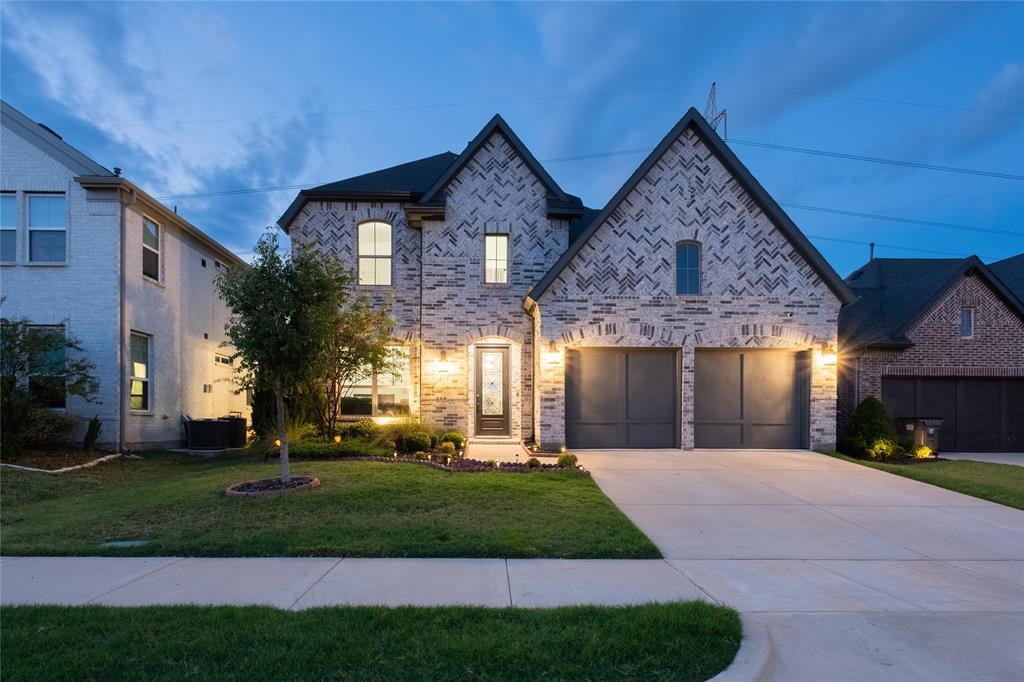 Two-story brick exterior featuring a herringbone pattern, arched entryway, and a two-car garage with paneled doors