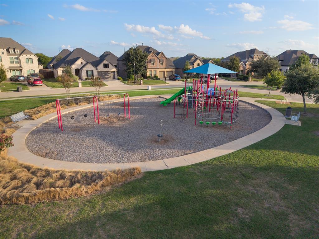 Recreational area featuring a gravel playground with built-in play structures, swings, a shade canopy, and concrete perimeter curbing