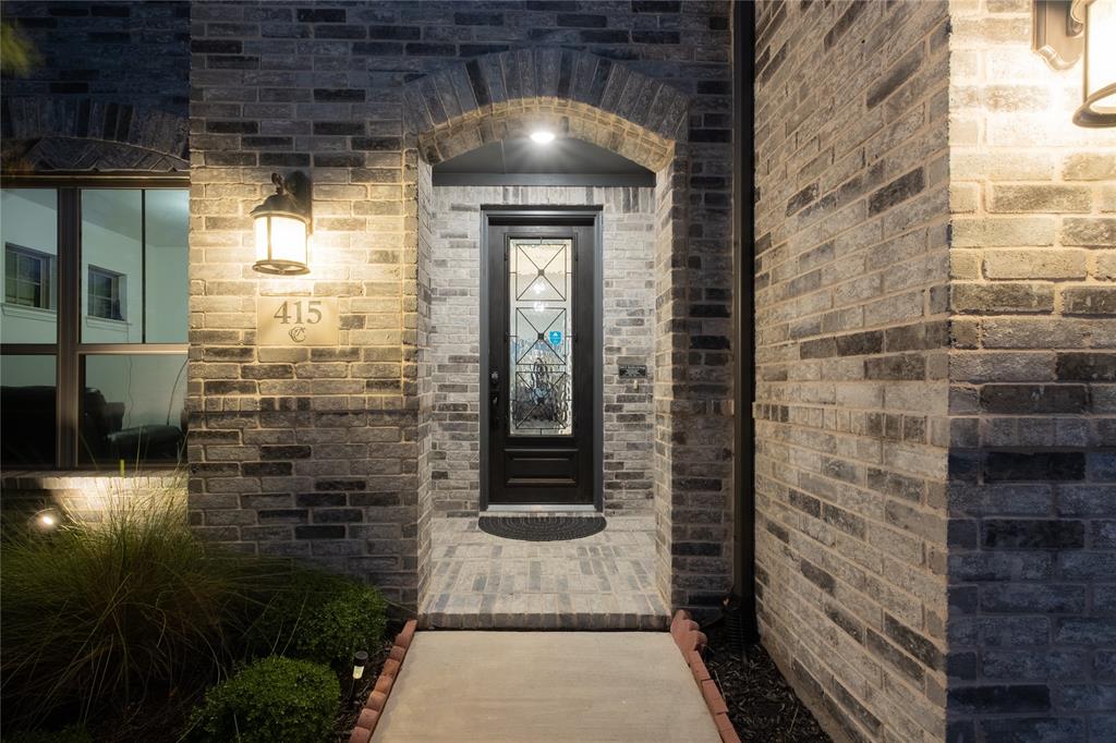 Exterior entryway featuring a multi-tonal brick facade, an arched masonry header, a dark-finished front door with decorative glass inlay, and wall-mounted exterior sconces