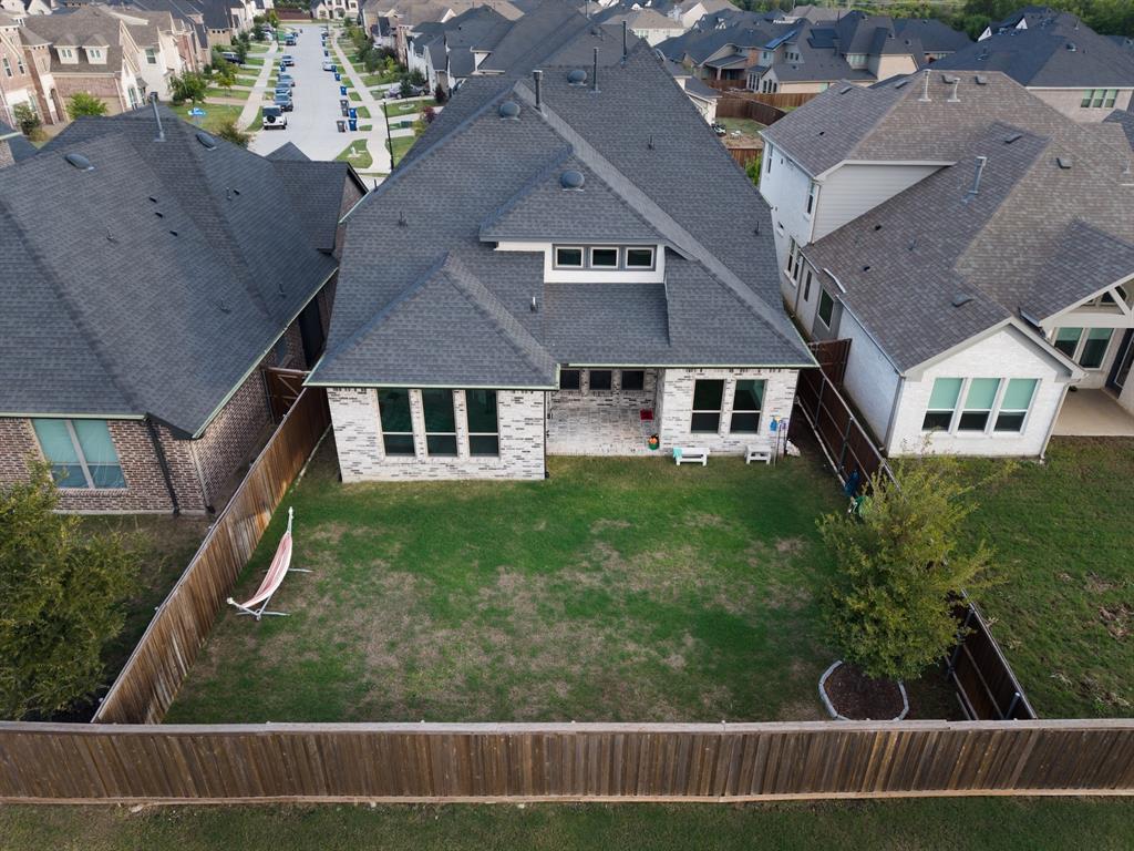 Aerial perspective of a multi-gabled residence featuring a light-toned brick facade, asphalt shingle roofing, a covered patio area, and a fully fenced backyard