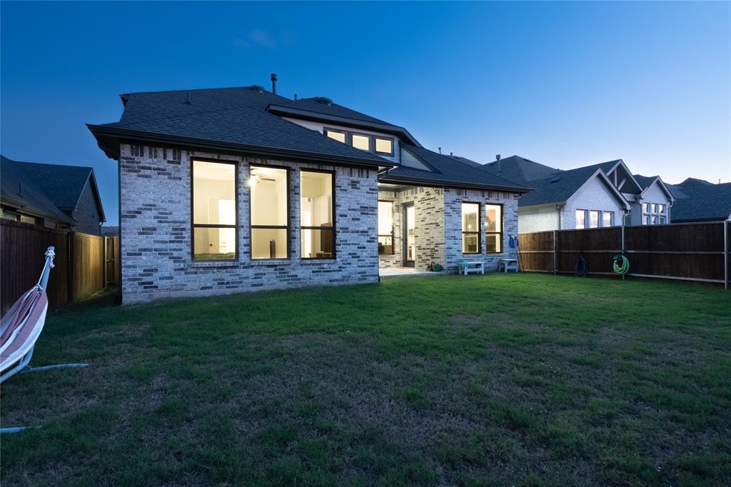 Rear elevation featuring brick masonry, large multi-pane windows, a covered patio, and wood privacy fencing surrounding the lawn