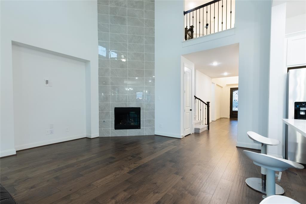 Double-height ceiling, floor-to-ceiling tile fireplace surround, wood-finish flooring, and iron stair railing