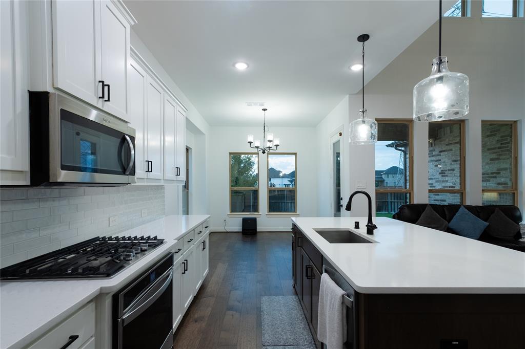 Kitchen featuring white shaker-style cabinetry, quartz countertops, a central island with a matte black faucet, stainless steel appliances, and wood-finish flooring