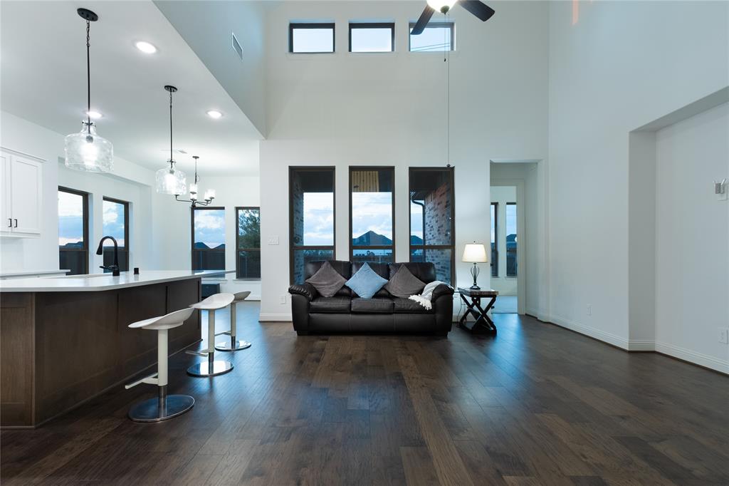 Open-concept space featuring double-height ceilings, wood-finish flooring, oversized windows, and a kitchen island with pendant lighting